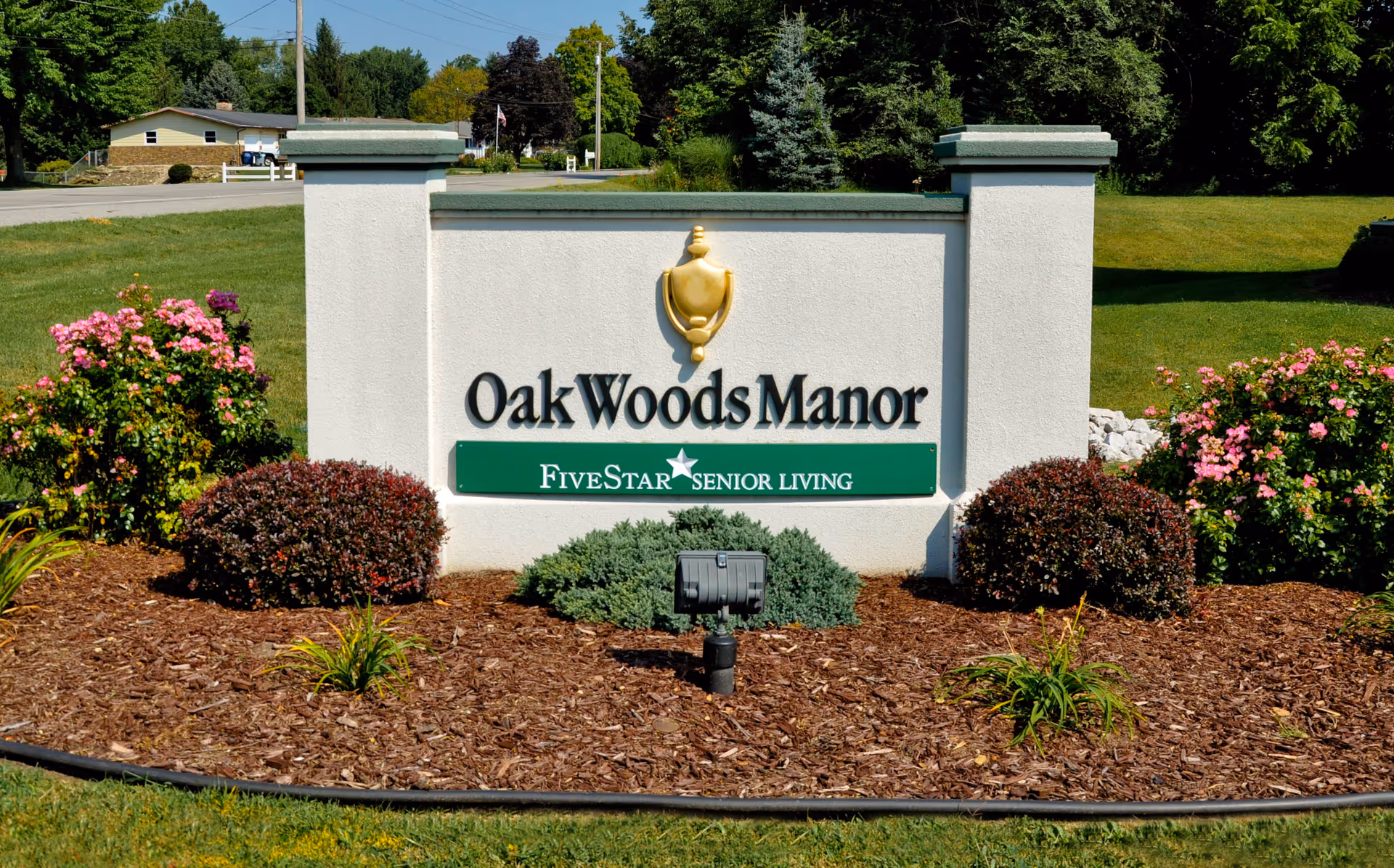 Entrance sign reading "Oak Woods Manor" with "FiveStar Senior Living" set in landscaped beds near a roadside.