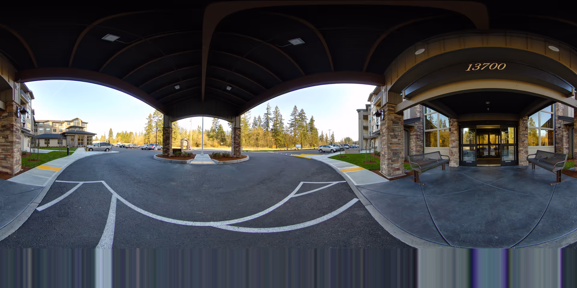 Covered circular driveway and main entrance of a senior living building with benches and the address 13700 above the entry.