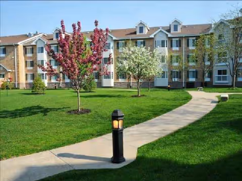 Front view of Cottage Grove Place senior living building with green lawn, walkway, and trees.