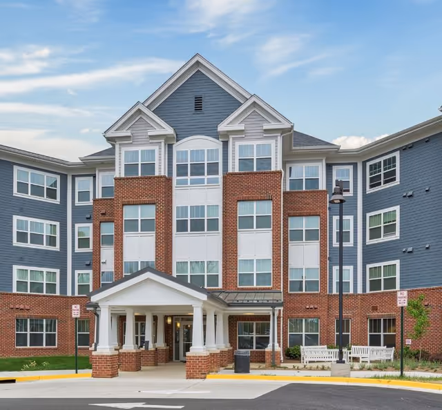 A blue-gray brick-and-siding senior residence exterior with a covered entrance.