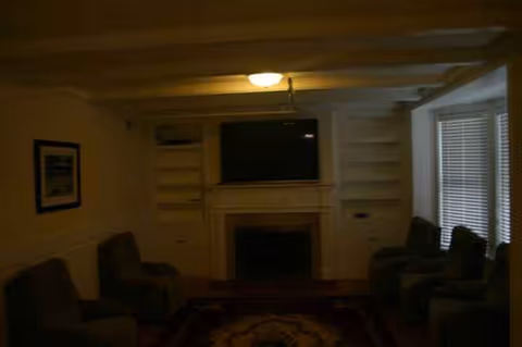 Dimly lit living room with built-in shelves, fireplace, TV, and multiple chairs.