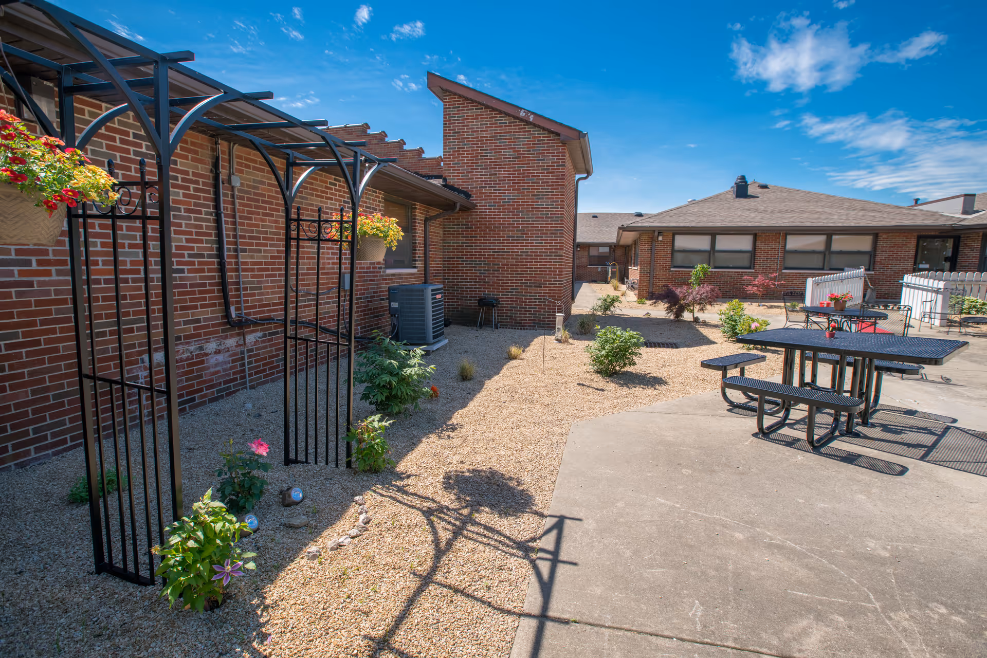 A landscaped outdoor area of Glen Meadows Nursing Center featuring a pergola, tables, and flower beds.