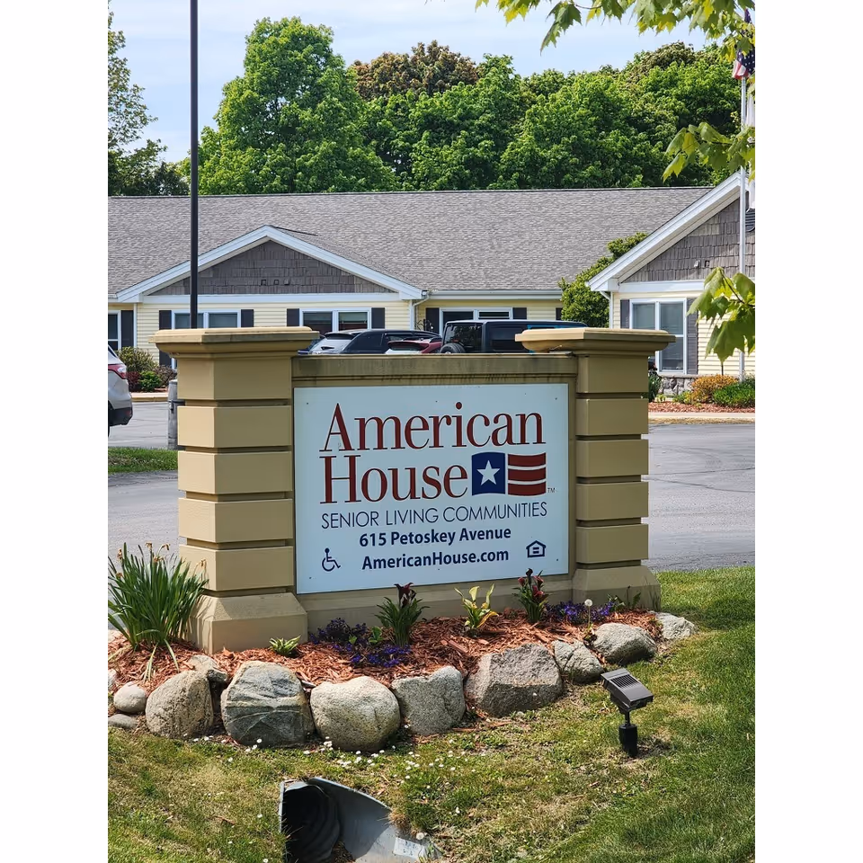 Sign for American House Charlevoix senior living facility with address and decorative landscaping.