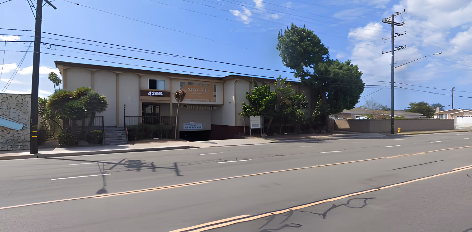 Two-story building front facing a multi-lane street with trees, entrance stairs, and a garage driveway.