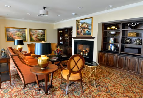 Cozy common living room with upholstered chairs, a fireplace, built-in bookshelves, and decorative lamps.
