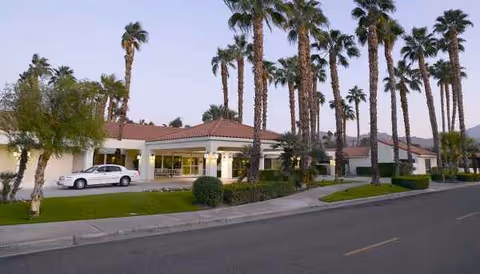 Exterior view of a senior living facility with palm trees and a curved driveway.