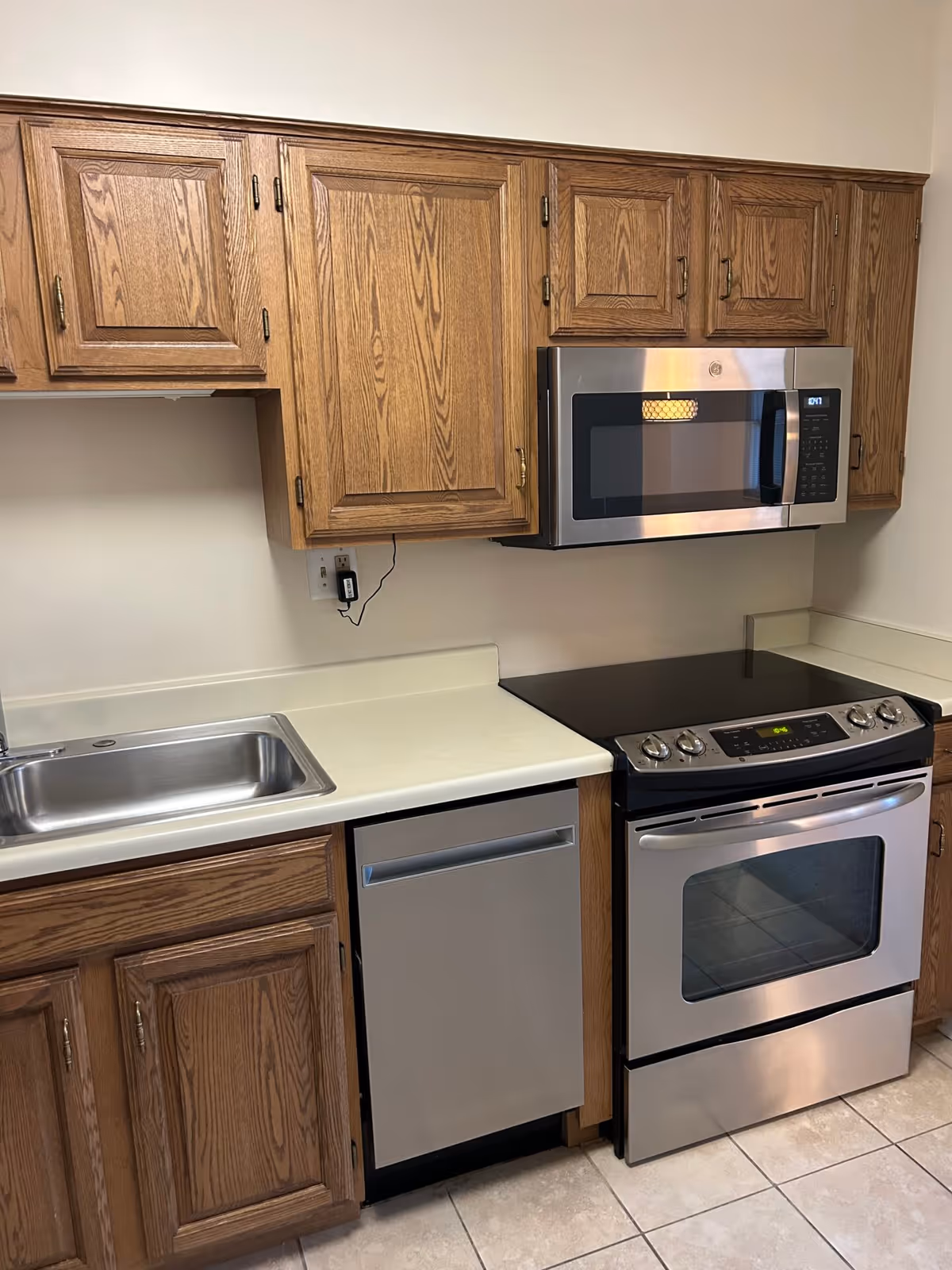 Kitchen with wooden cabinets, stainless steel microwave, oven, dishwasher, and a single-basin sink over tiled floor.