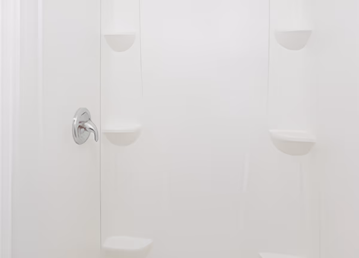 A clean, white shower stall with built-in corner shelves and a silver faucet handle on the left side.