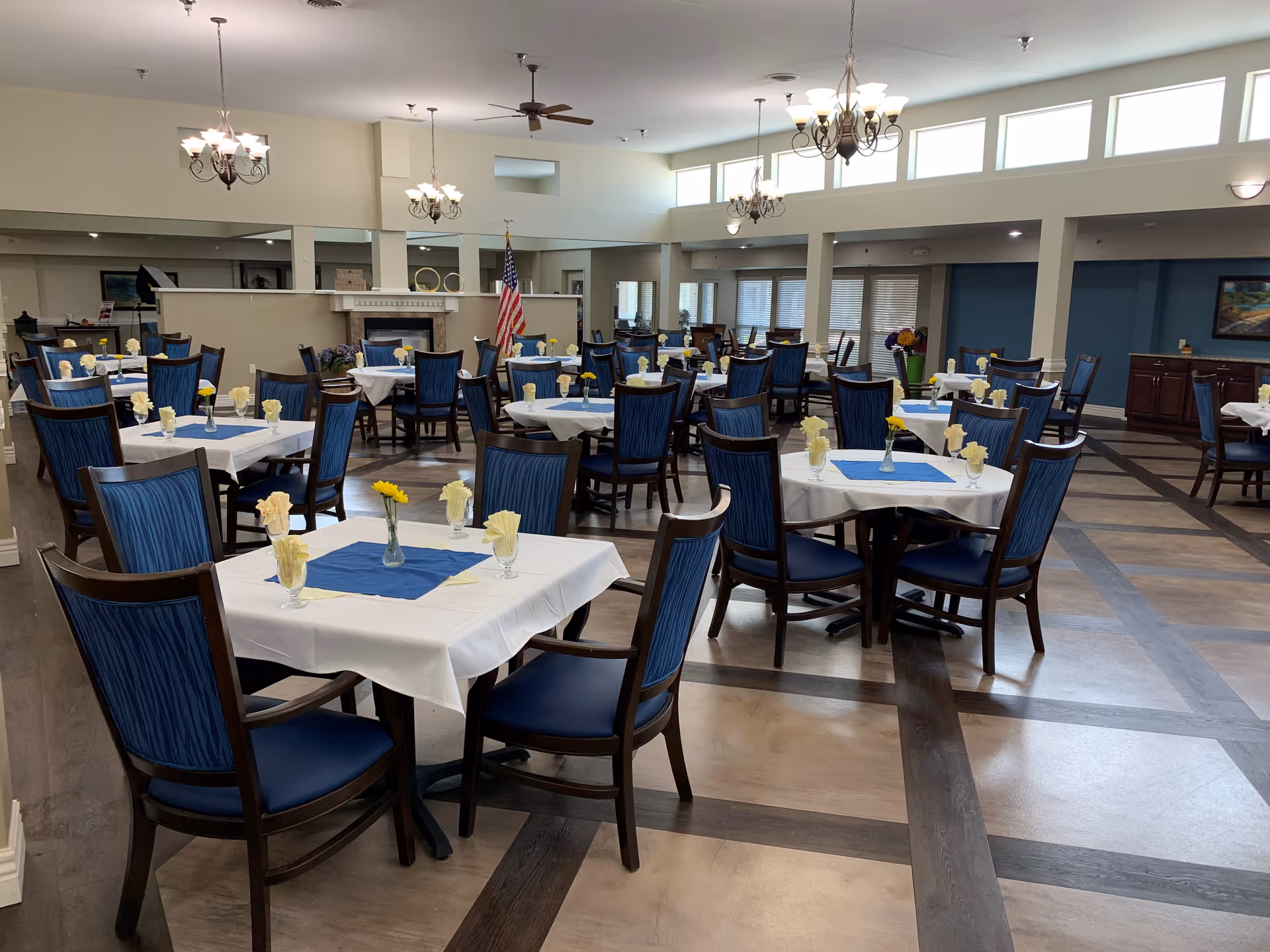 Spacious dining hall with white tablecloth tables, blue chairs, and floral centerpieces.