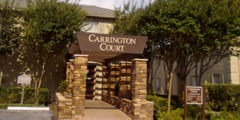 Entrance to Carrington Court Assisted Living and Memory Care facility with a stone pillar archway and surrounding trees and shrubs.