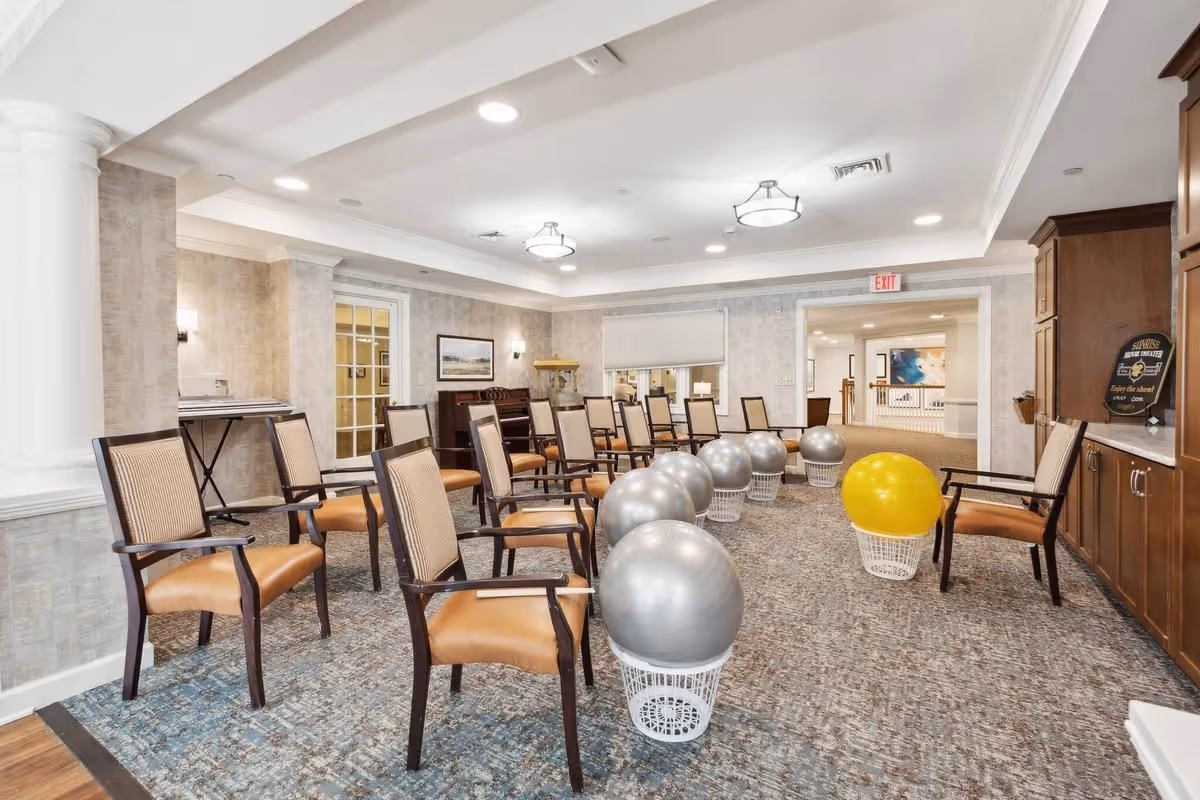 Bright communal activity room with rows of chairs and several exercise balls placed in baskets.