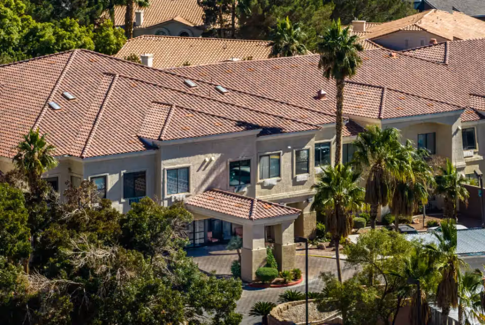 Aerial view of a two-story building with terracotta tile roofs, palm trees, and a covered main entrance.