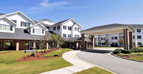 White multi-story senior living facility with curved driveway and manicured landscaping.