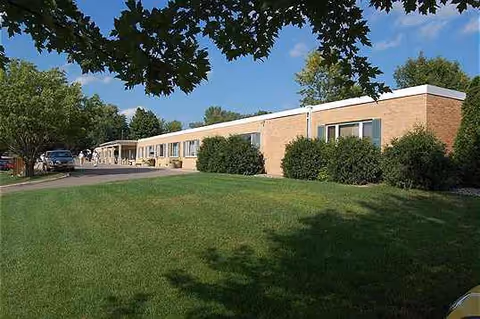 Exterior view of Pleasant Manor senior living facility with brick building, green lawn, and trees.