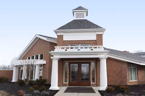 Front entrance of a brick senior living facility with white columns and a cupola.