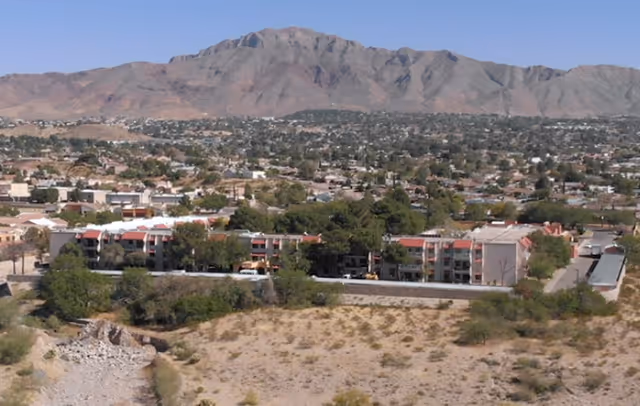 Aerial view of a senior living complex and surrounding desert with a town and mountains in the background.