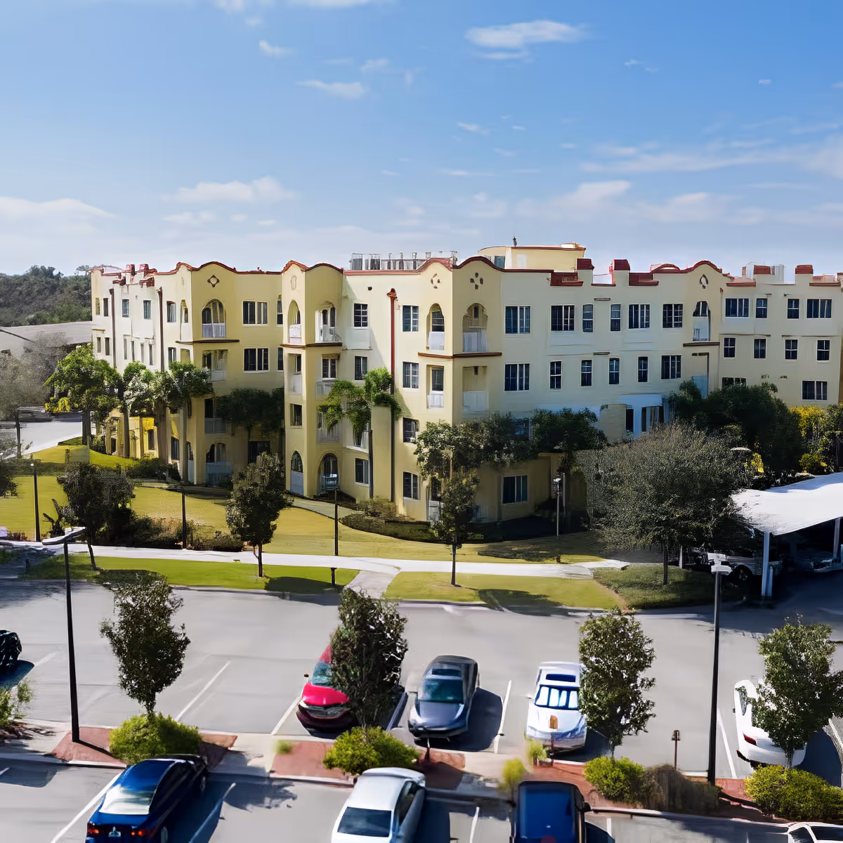 Exterior front view of a multi-story yellow senior living building with landscaped grounds and parked cars in the foreground.