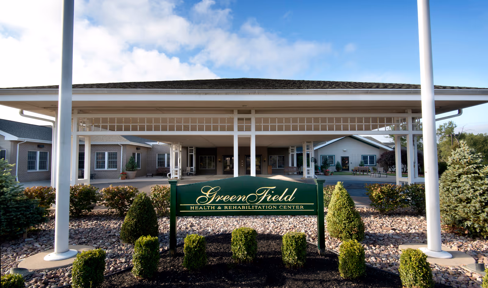 Covered entrance and porte-cochère of the GreenField Health & Rehabilitation Center with a green sign and landscaped shrubs in front.