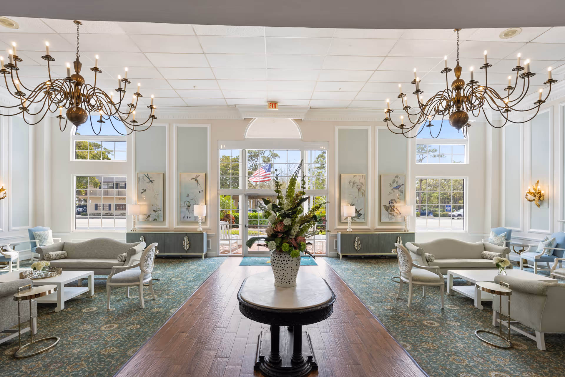 Bright lobby seating area with chandeliers, sofas, and a central floral arrangement.