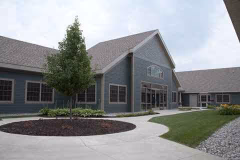 Exterior view of a modern senior living facility with curved walkway and landscaped entrance.