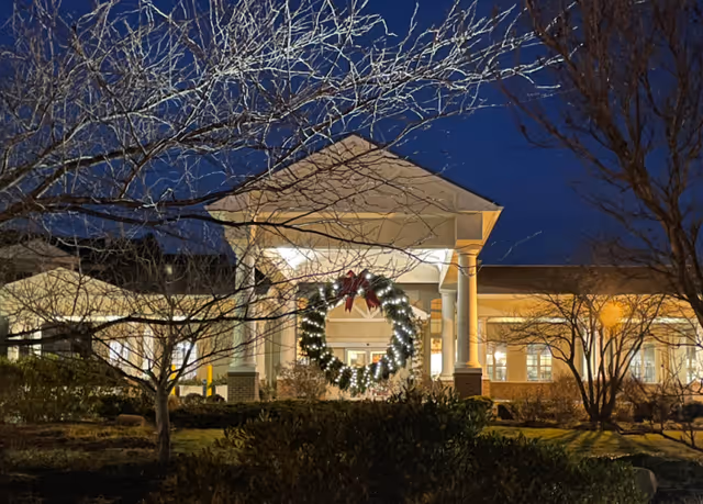 Front entrance of a building at night decorated with a large illuminated holiday wreath and columns.