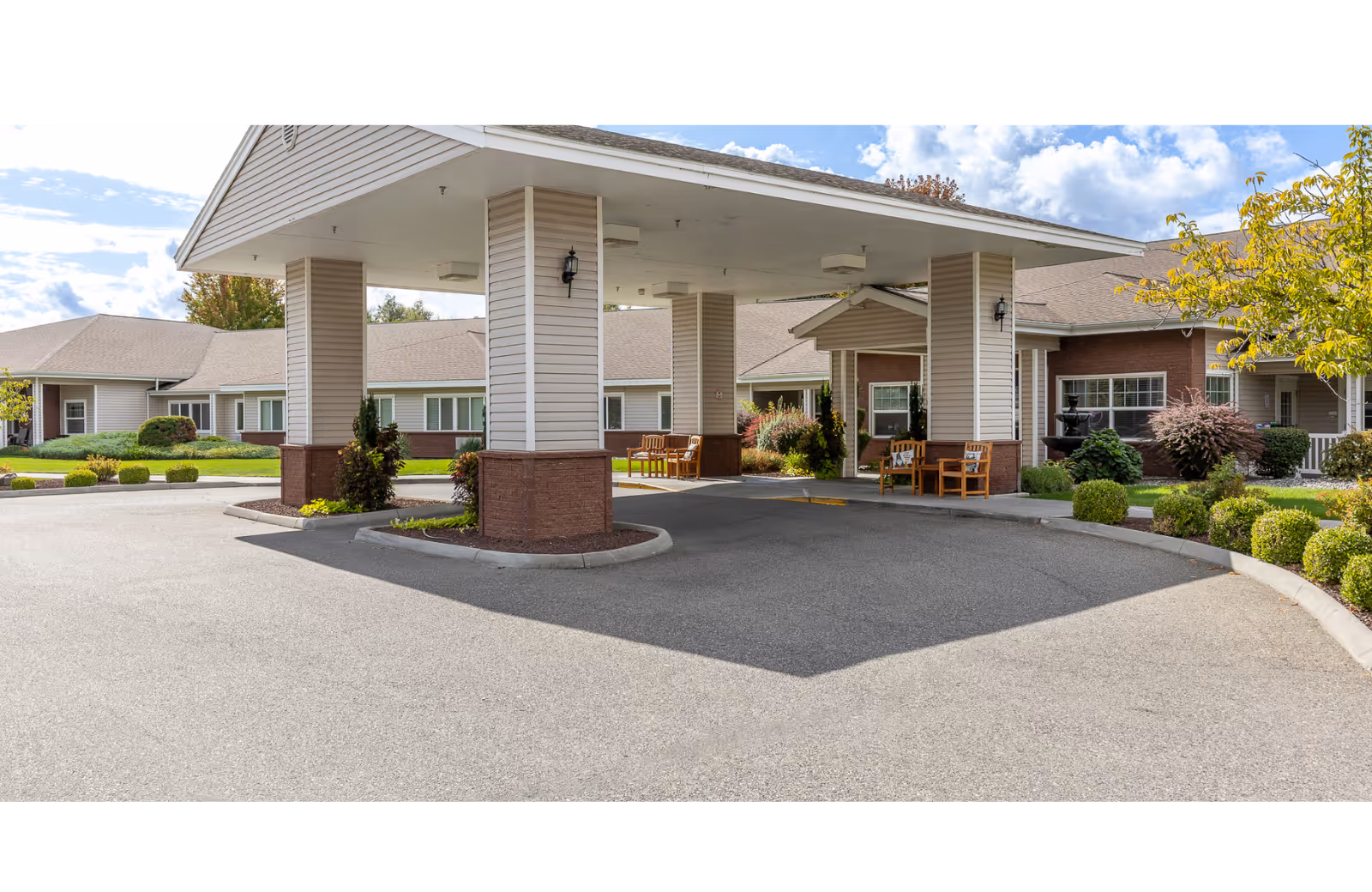 Covered entrance/porte-cochere of a single-story senior living facility with benches and landscaped grounds.