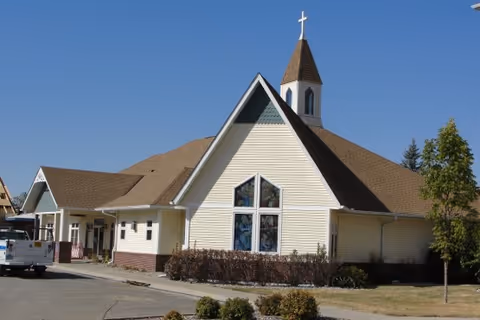 Single-story senior living building with a steep gabled facade, a large cross-shaped stained-glass window and a small steeple topped by a cross.