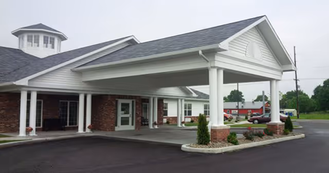 Covered porte-cochère entrance with white columns and brick facade in front of a single-story care facility.