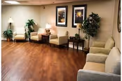 Common seating area with armchairs, side tables, lamps, framed artwork and potted plants on a wood floor.