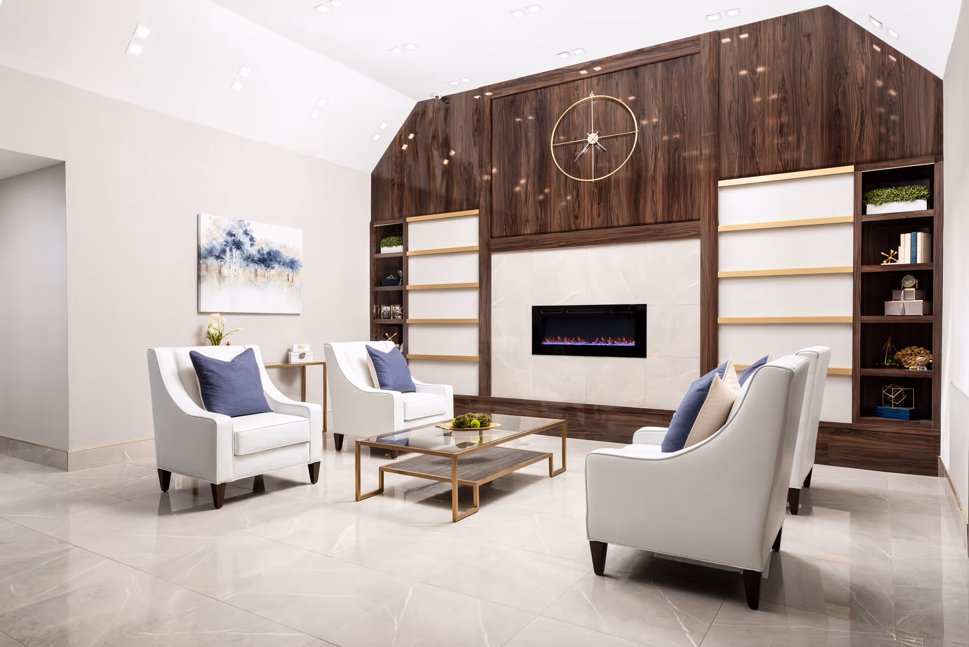 A modern sitting area with white armchairs, a glass coffee table, and a built-in fireplace in a wood-paneled wall.