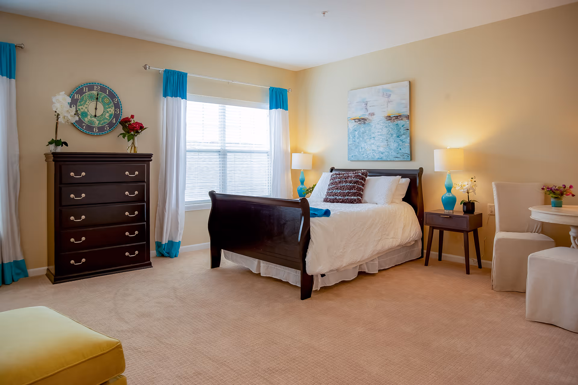 Well-lit bedroom with a dark wood sleigh bed, matching dresser, bedside tables with blue lamps, and a window with white and turquoise curtains.