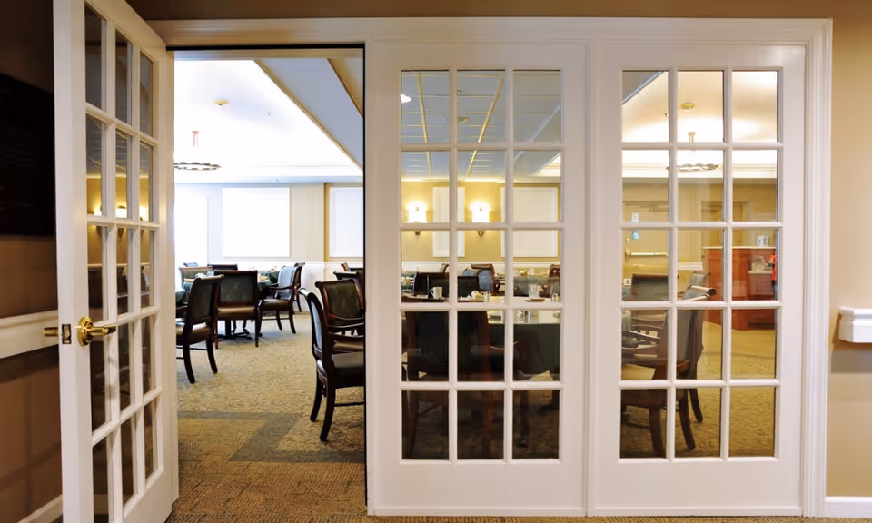 White glass-paneled doors open into a well-lit dining room with round tables and chairs.