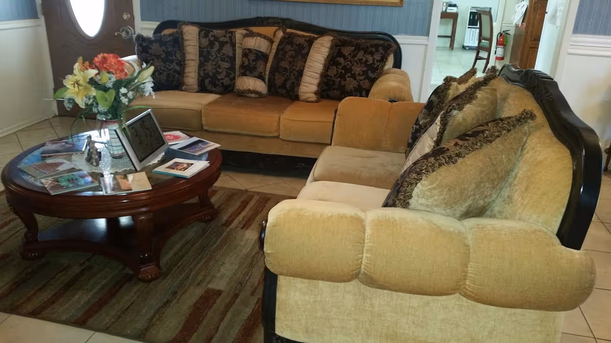 A living room with two upholstered sofas, a round wooden coffee table holding magazines and a floral arrangement, and a front door in the background.