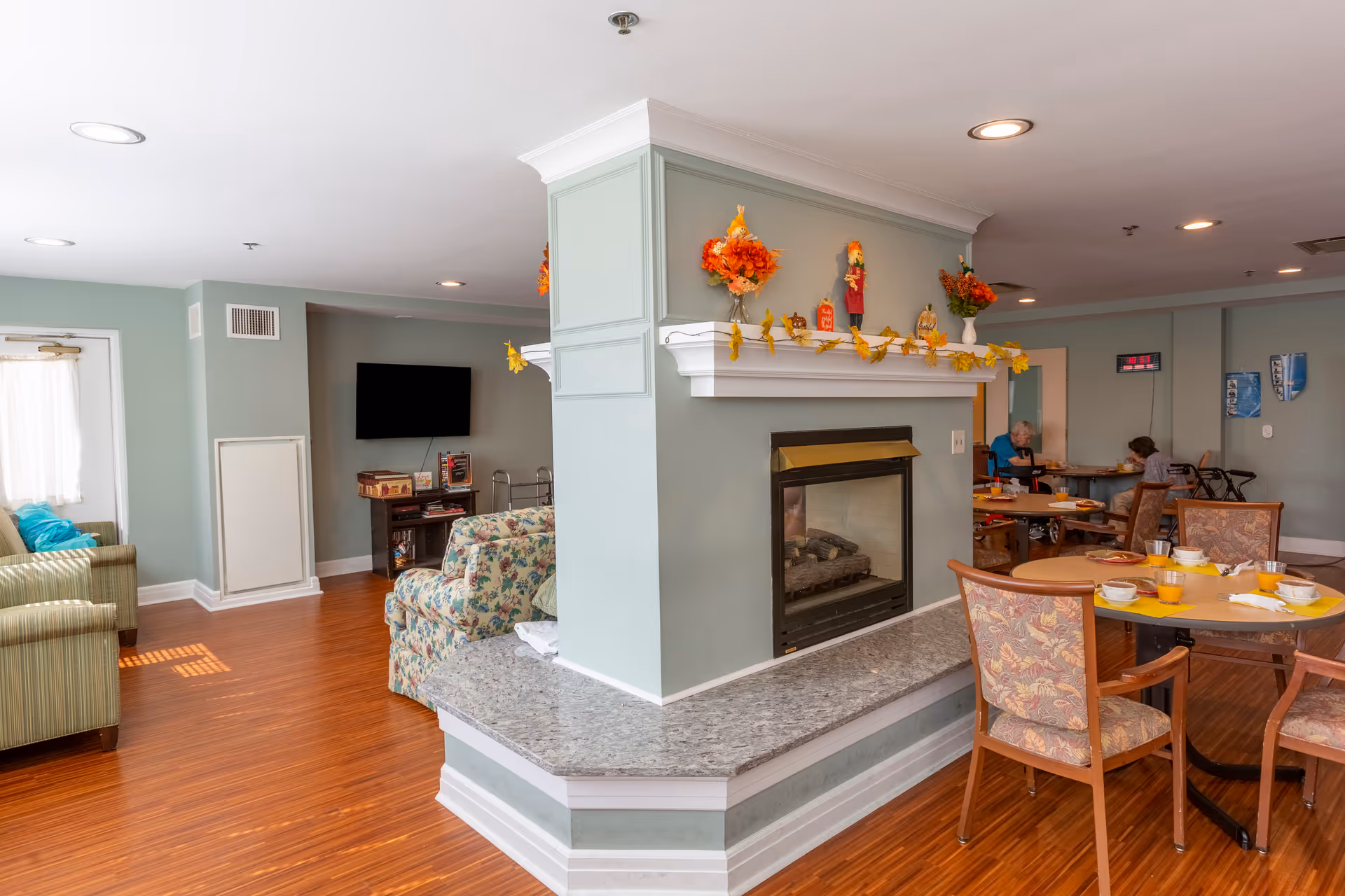 Communal dining and lounge area with a central fireplace, round dining tables set with dishes, and seating.