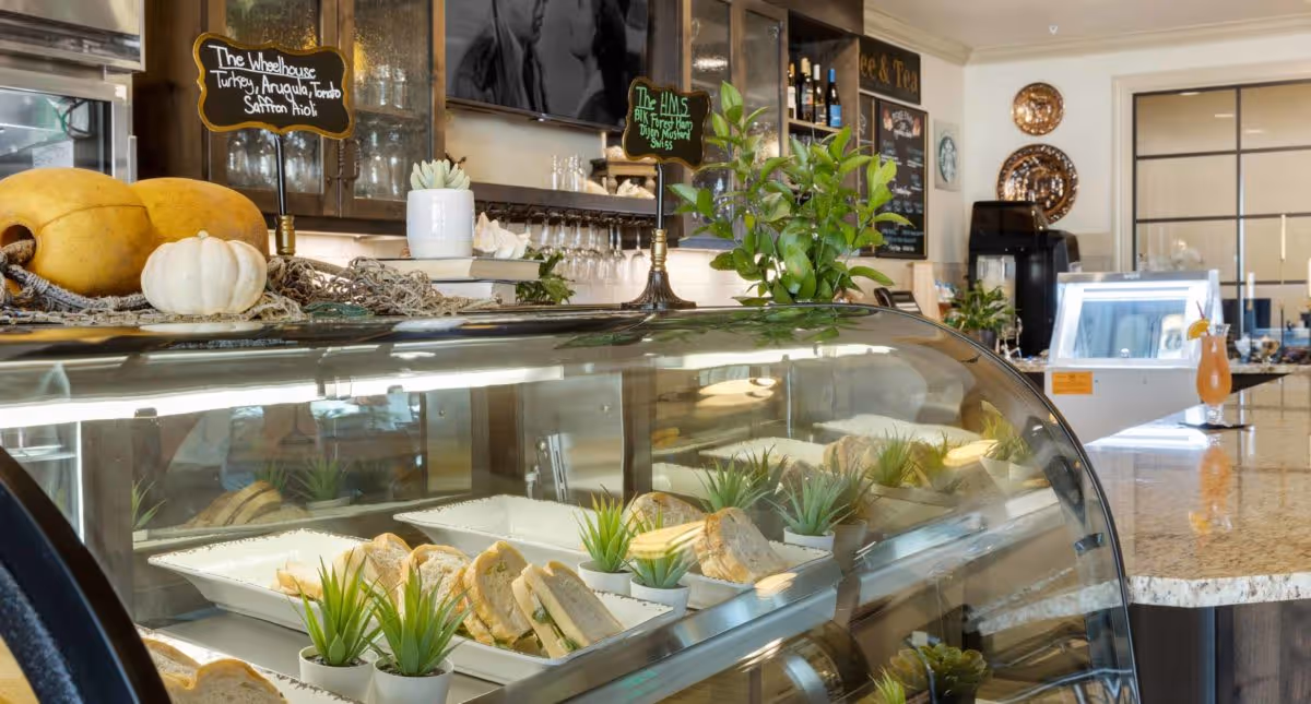 A cafe-style display case with sandwiches and small plants on a countertop in a dining area with chalkboard menus and decorative pumpkins.