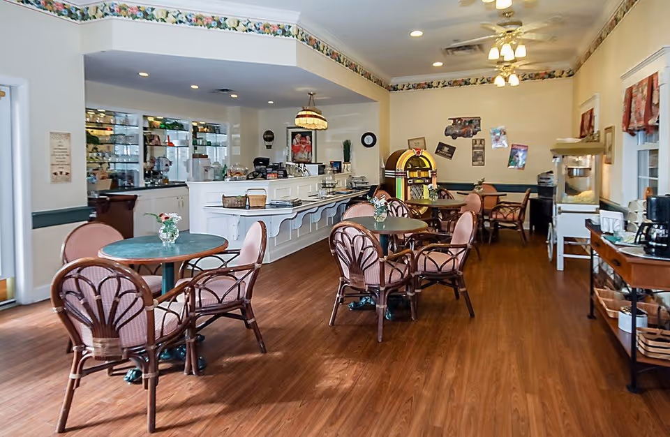 Bright communal dining room with round tables and wicker chairs, a service counter, jukebox and snack station.