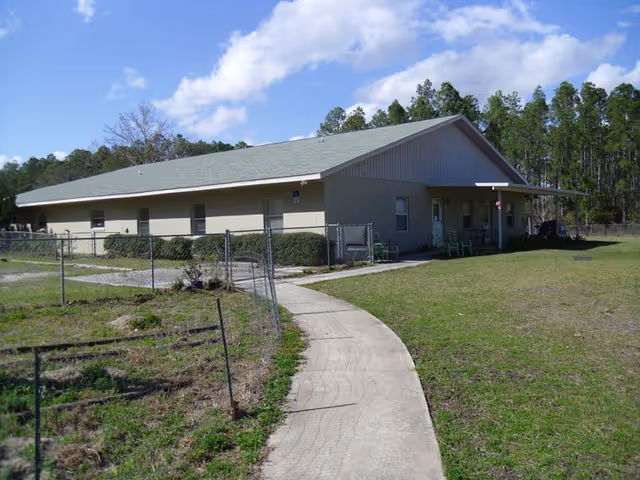 Exterior of Pomona Park ALF showing curved path, fence, and grassy yard.