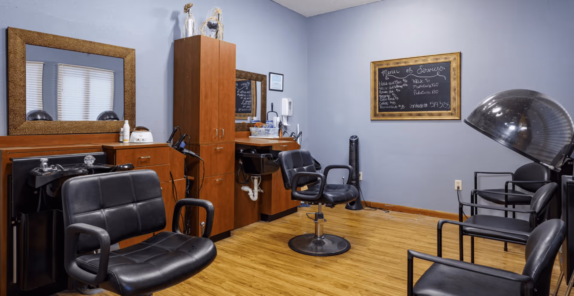 Interior salon room with styling chairs, shampoo sinks, mirrors, a hooded hair dryer, and wooden cabinets.
