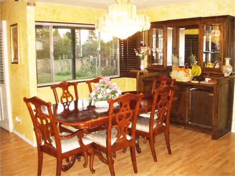 A wood dining set with six chairs, chandelier, and a sideboard in a yellow-walled dining room.