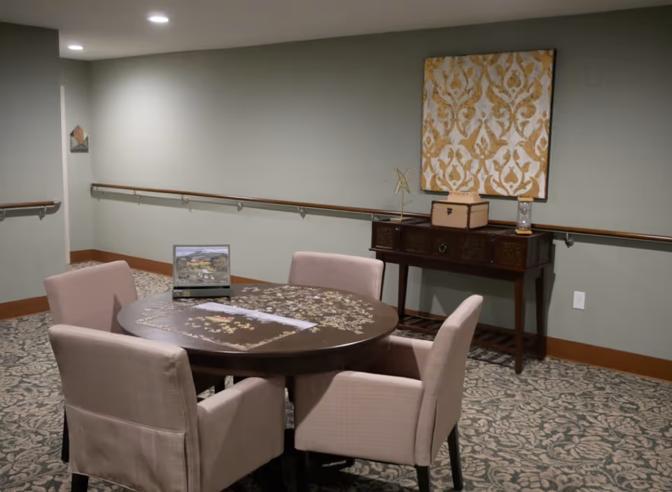 A round wooden table with four beige upholstered chairs in a softly lit dining area.