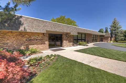 Brick senior living facility exterior with entrance, glass doors, and manicured lawn.