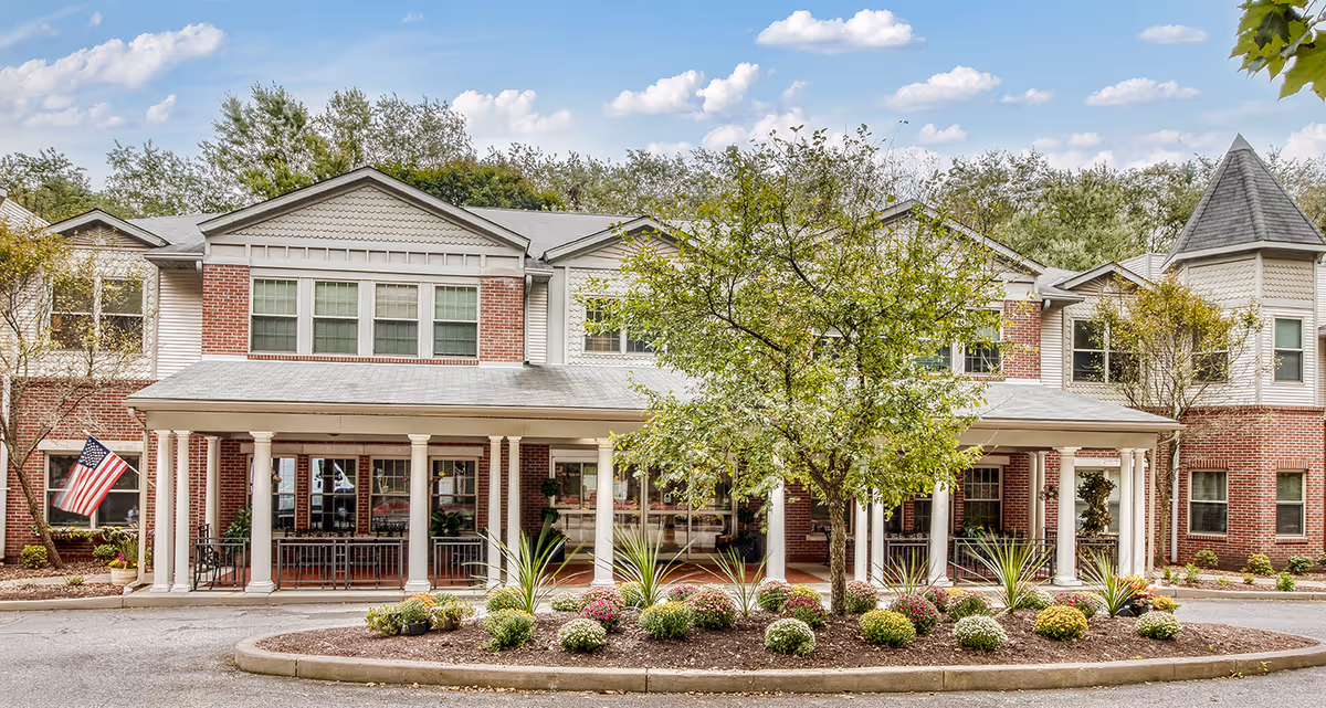 Exterior view of Juniper Village at Forest Hills with a covered entrance, trees, and landscaping.