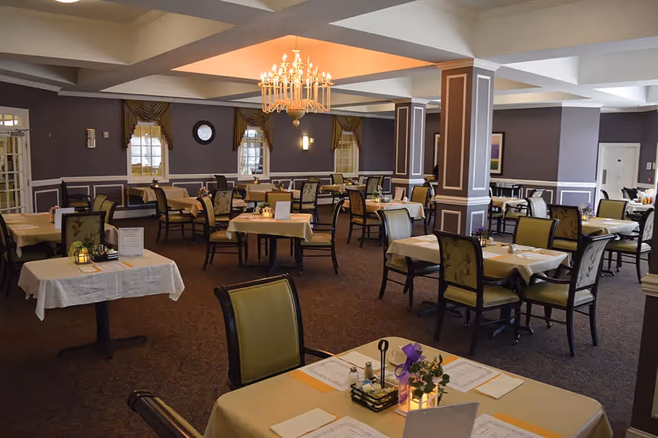 Spacious dining room with multiple set tables and chairs, a central chandelier, and purple-accented walls.