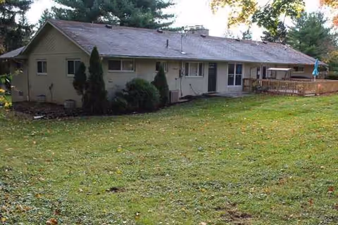 Single-story senior living home with a grassy yard and a wooden deck.