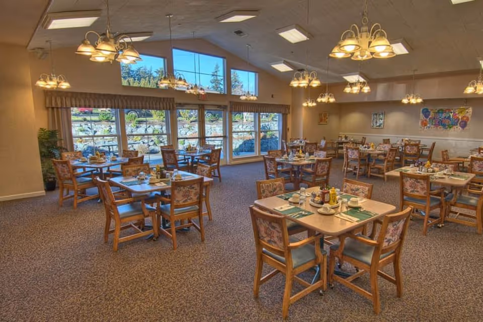 Interior view of the dining room at Chandler's Square, featuring tables set for meals, large windows allowing natural light, and decorative lighting fixtures.
