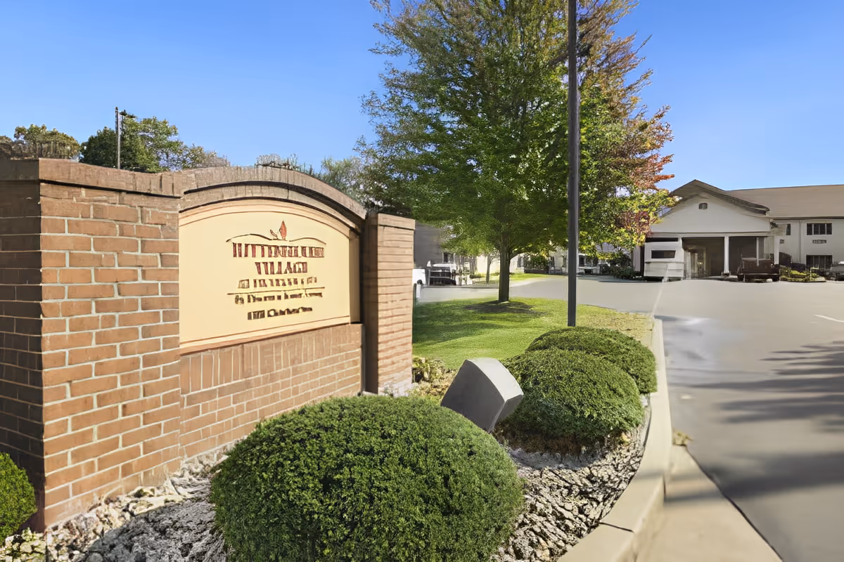 Brick entrance sign and landscaped driveway leading to a senior living facility building under a clear sky.