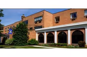 Exterior view of a brick senior living building with arched windows, a small lawn, and a blue sign near the entrance.