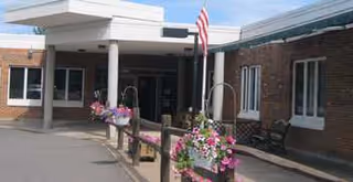 Entrance of Oaks Assisted Living building with brick exterior, flag, and flower planters.