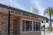 Exterior view of Atlantic Memorial Healthcare Center building with stone and beige walls, a street lamp, palm trees, and a clear sky.