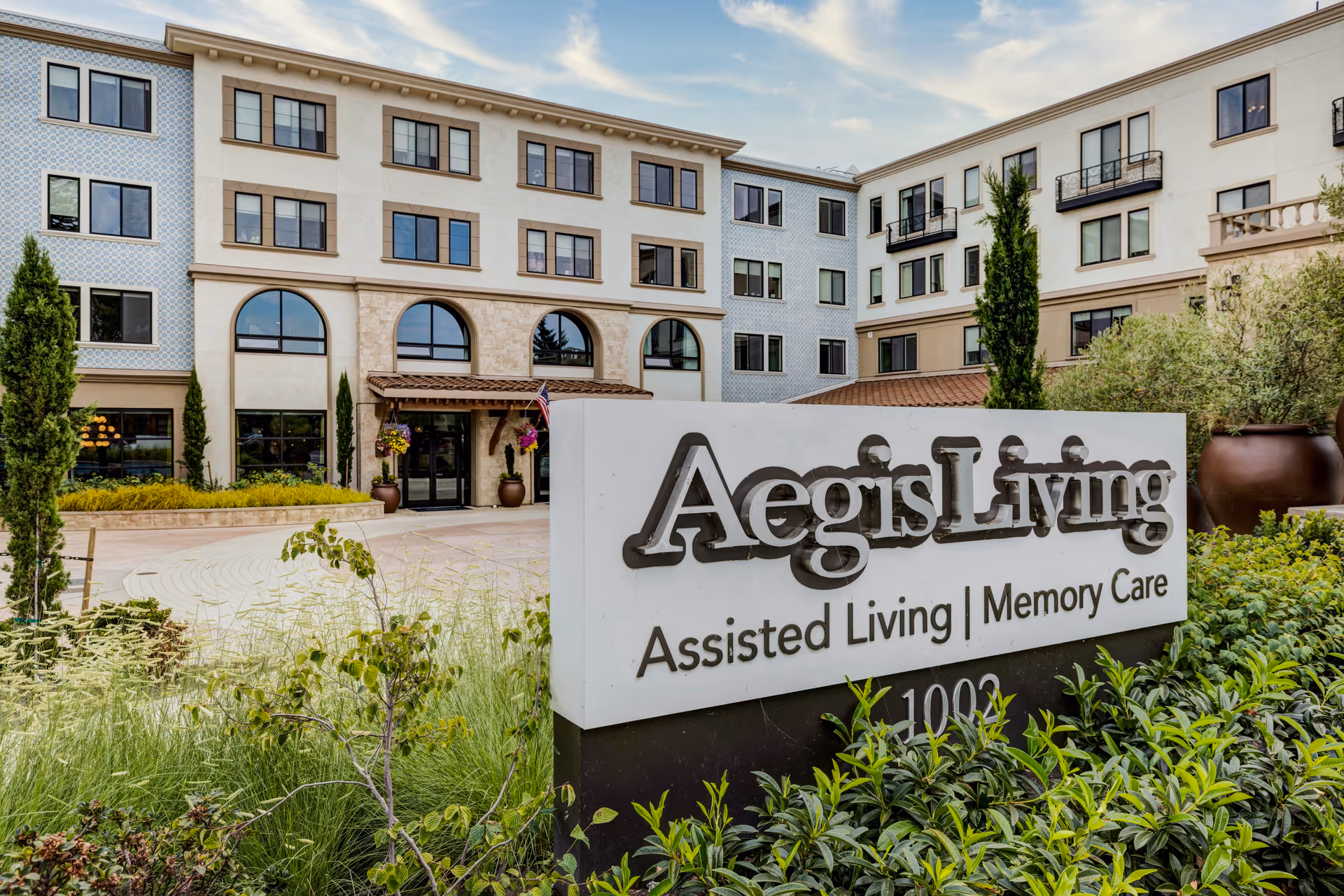 Front exterior of Aegis Living assisted living and memory care building with a large sign in the landscaped entrance.
